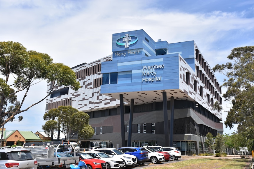 A blue building with Werribee Mercy Hospital sign surrounded by parked cars.