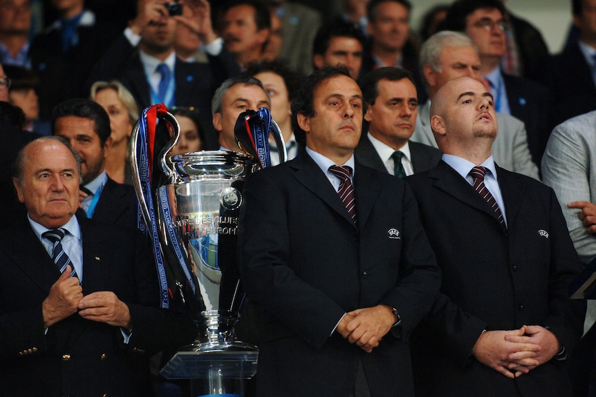 Three men stand next to a trophy during a football match.