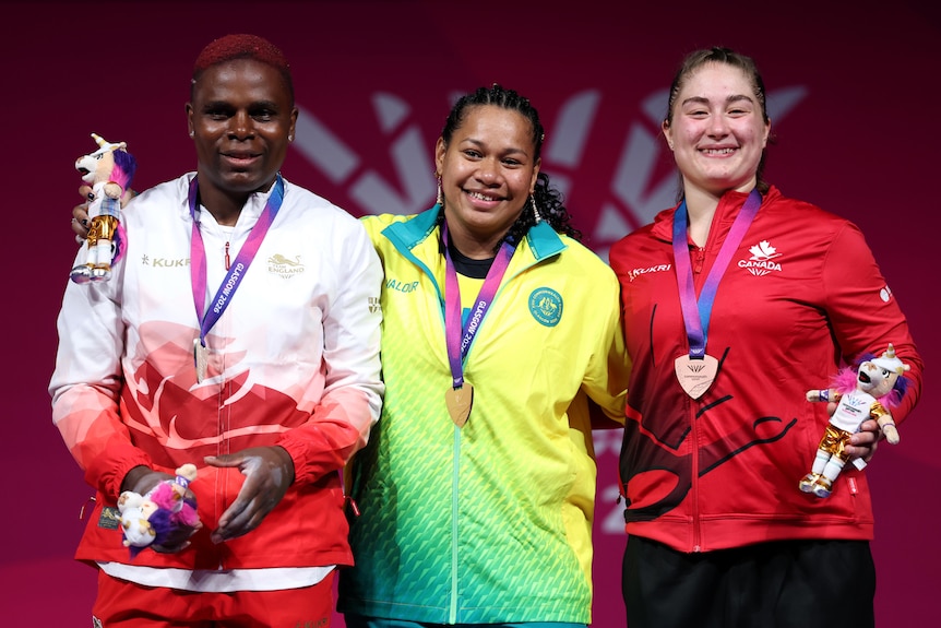 Three women stand on a podium and show off their medals.