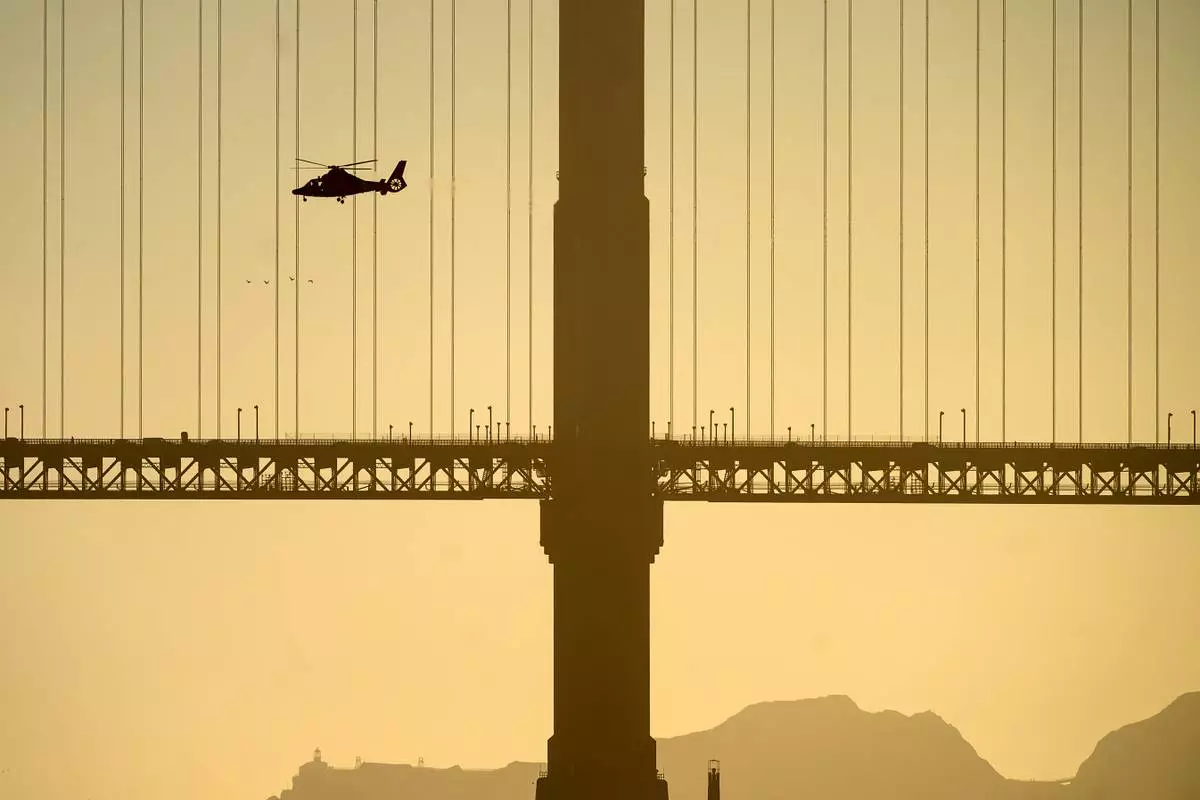 A helicopter flies past the Golden Gate Bridge while searching for missing victims after a boat accident near Alcatraz Island off San Francisco, Tuesday, July 14, 2026. (AP Photo/Noah Berger)