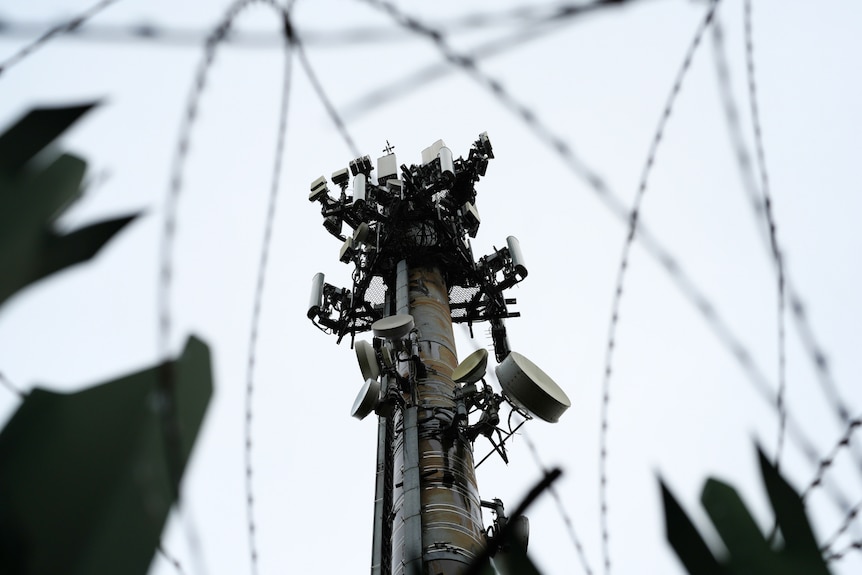 crowded mobile phone tower viewed up from the ground, behind barbed wire