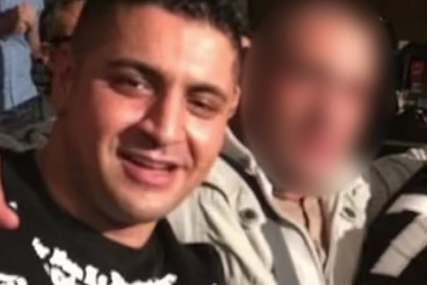 Kazem Hamad wearing a black T-shirt sitting next to two unidentified men with their faces blurred.