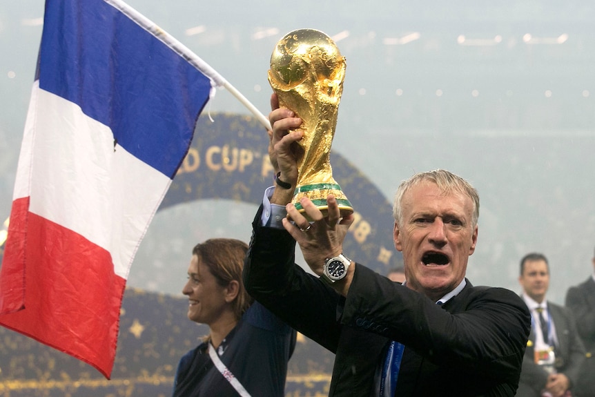 A coach holds up a golden trophy in front of the French flag.