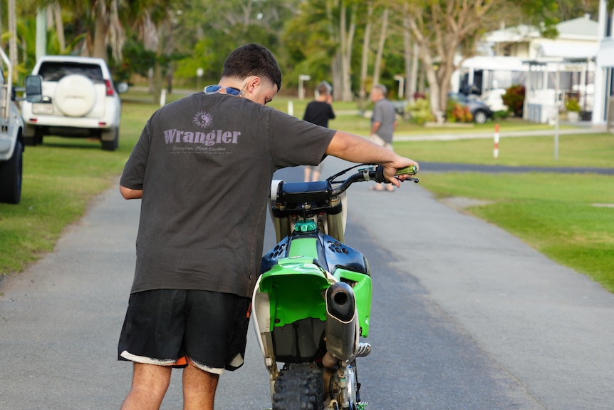 A young man walking a bike down a street