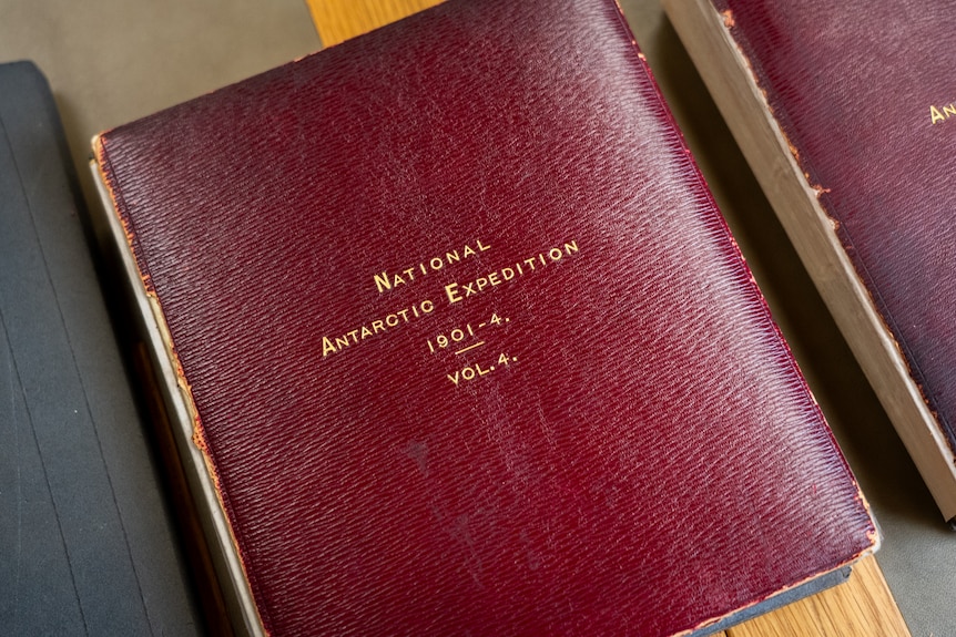 A leather bound book sits on a desk with gold lettering that reads: National Antarctic Expedition 1901-4