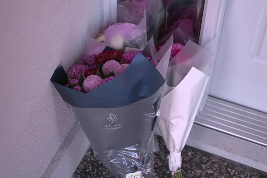 Two bunches of purple flowers resting against the front door of a house.