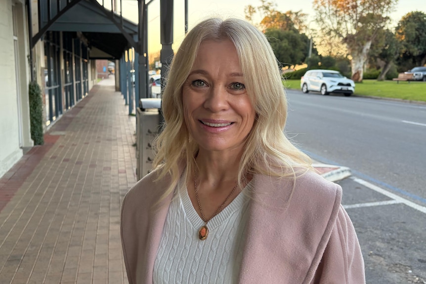A blond lady in a pink cardigan looks at the camera outside of Tailem Bend Town Hall