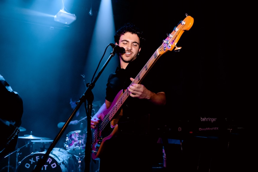 A young man sings on stage holding a guitar under a spotlight.