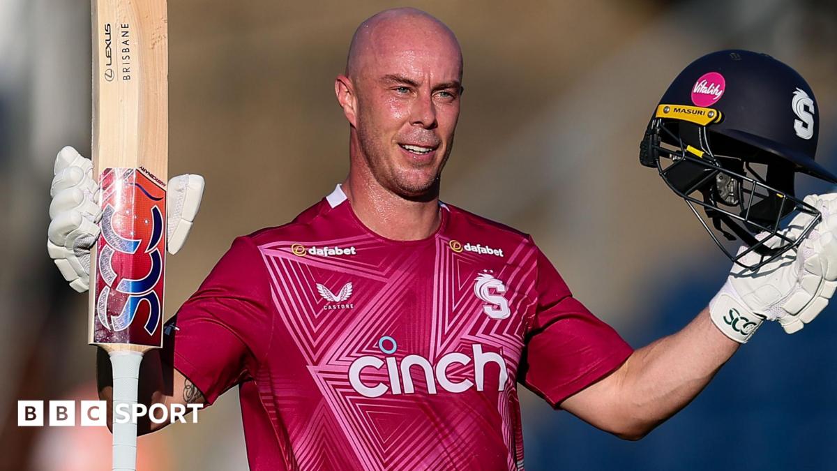 Chris Lynn, wearing Northamptonshire's red shirt, raises his bat and helmet to celebrate scoring a century against Glamorgan