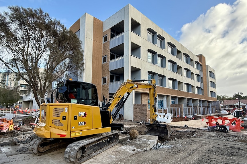 A bulldozer sits on broken ground next to tower block apartment