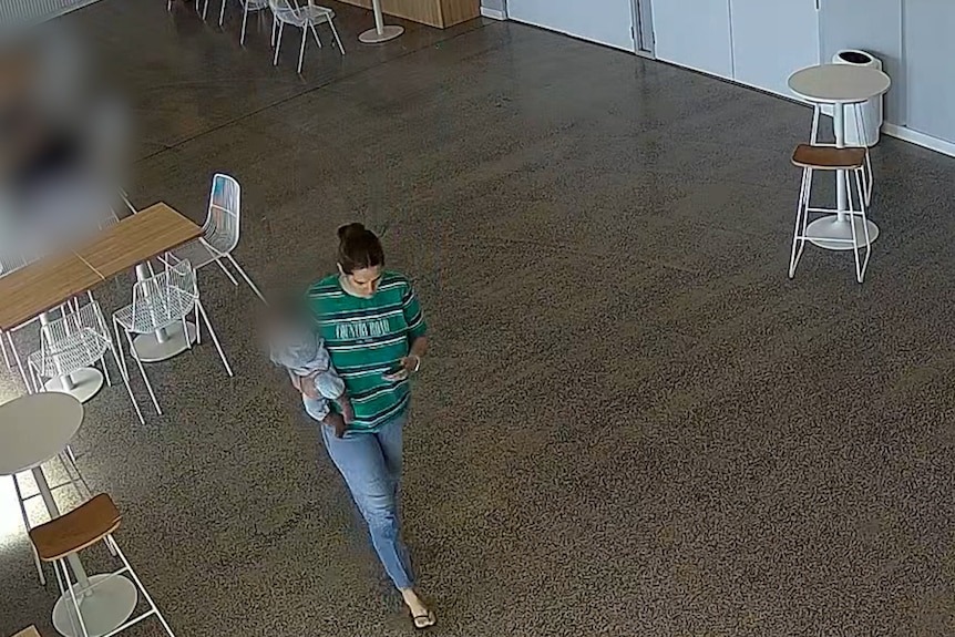 A CCTV image of a dark-haired woman carrying a baby through a cafe.