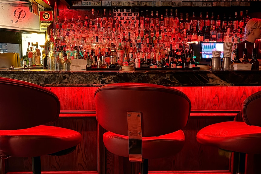 Bottles behind the bar , illuminated by red light. Empty bar stools in foreground