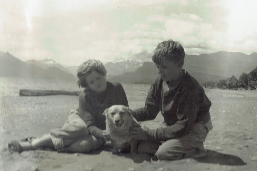 Black and white image young boy and girl sitting on the sand with a dog between them