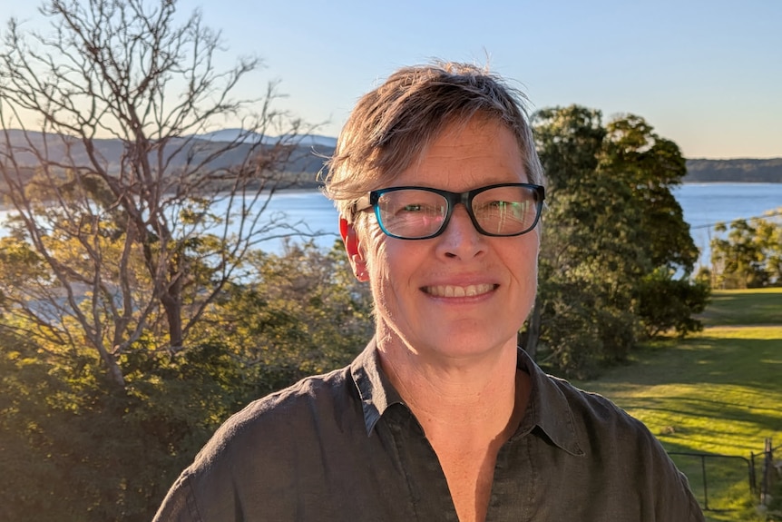 A woman with short hair, wearing glasses, standing near a body of water.