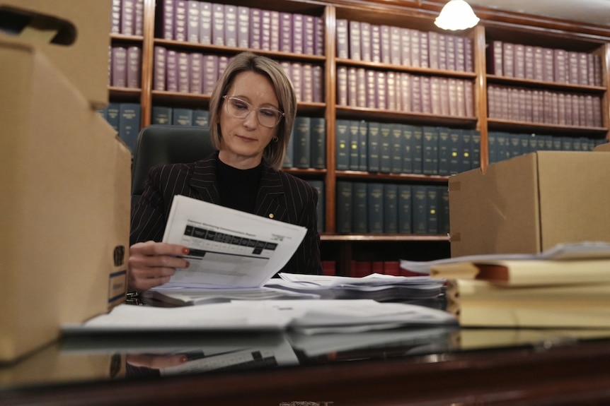 A woman at her desk examines paperwork with a bookshelf in the background