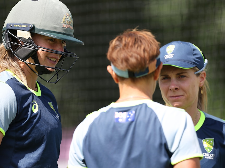Three cricketers talk during training.