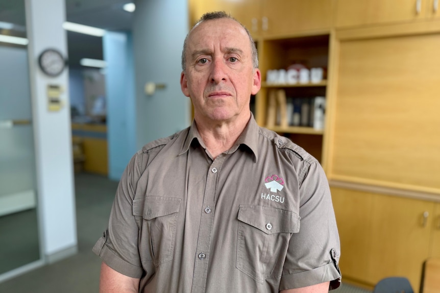 A portrait of a man wearing a khaki button-up shirt.