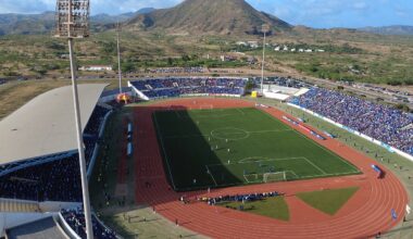 Aerial view of Cabo Verde’s Estádio Nacional filled with supporters during an international football match, with mountains rising behind the stadium as play unfolds on the pitch.