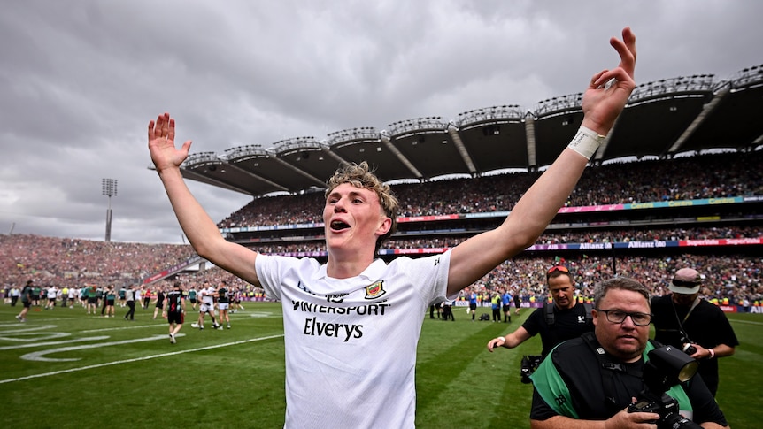 A Mayo Gaelic footballer stands on the pitch with arms outstretched after his team wins the All-Ireland football final.