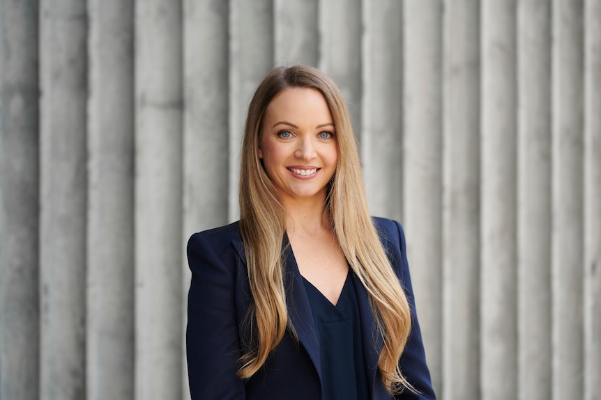 A woman with long blonde hair wearing a navy shirt and blazer. 