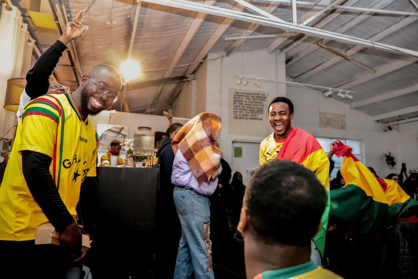 A man wearing a yellow t-shirt with red and green stripes and another draped in a yellow, red and green flag dance and smile.