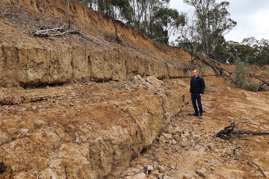 A man looks at a steep, dry riverbank twice his height