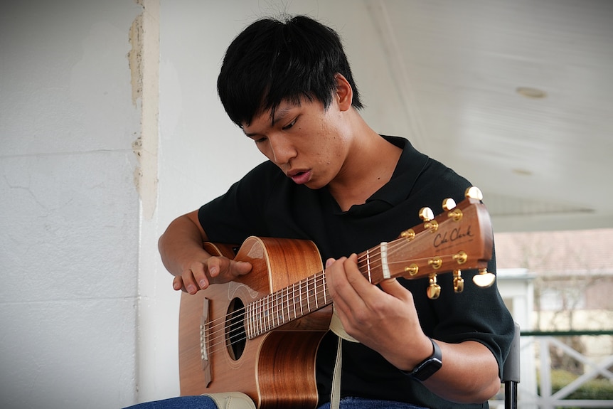 A young man with black hair playing guitar.