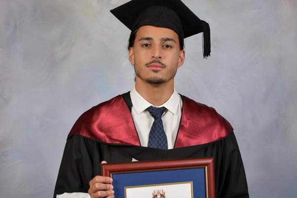 Mr Joseph wearing a graduating gown and holding frame