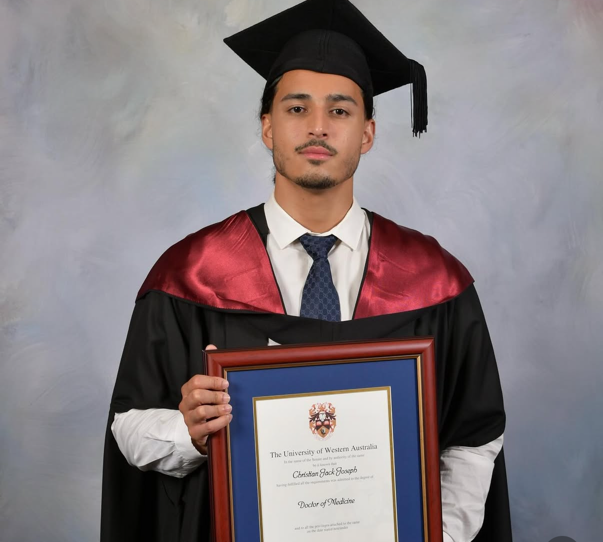 Mr Joseph wearing a graduating gown and holding frame