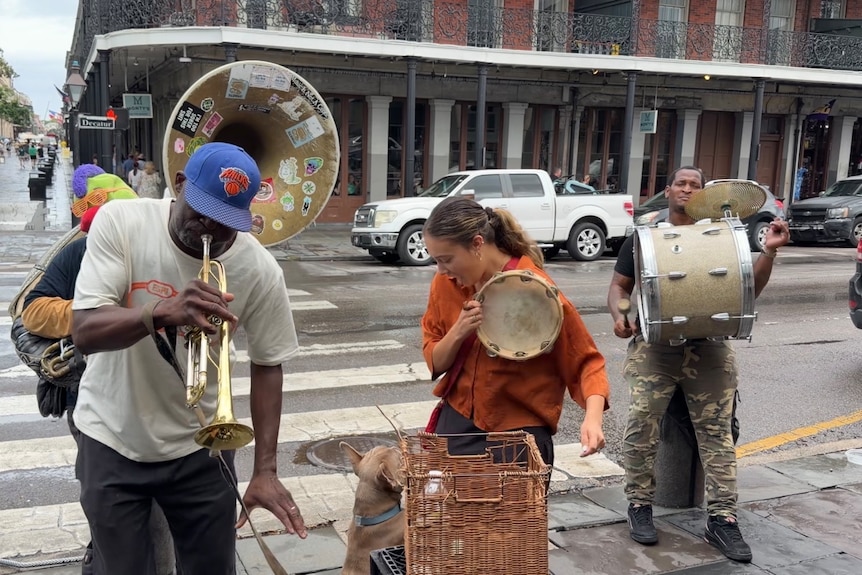 Mikaela holds a tambourine on the street with other performers playing instruments.
