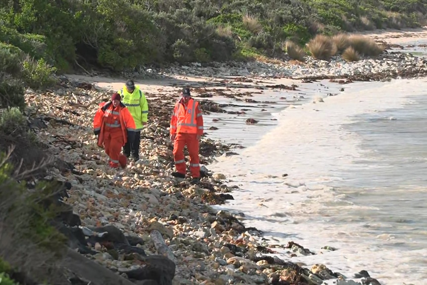 SES volunteers walk along a rocky beach with calm waters