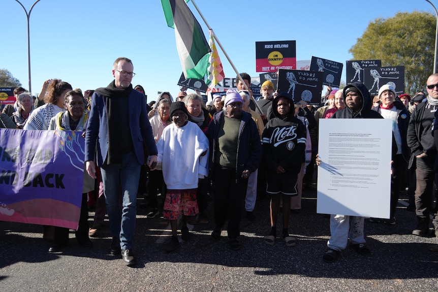 A large group of protesters walking down a wide road, holding signs and flags.