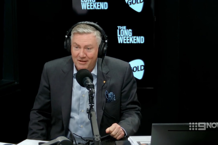 McGuire in a suit speaking into a microphone, wearing headphones in a radio booth.