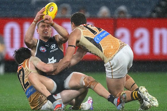 Patrick Cripps of the Blues handballs whilst being tackled.