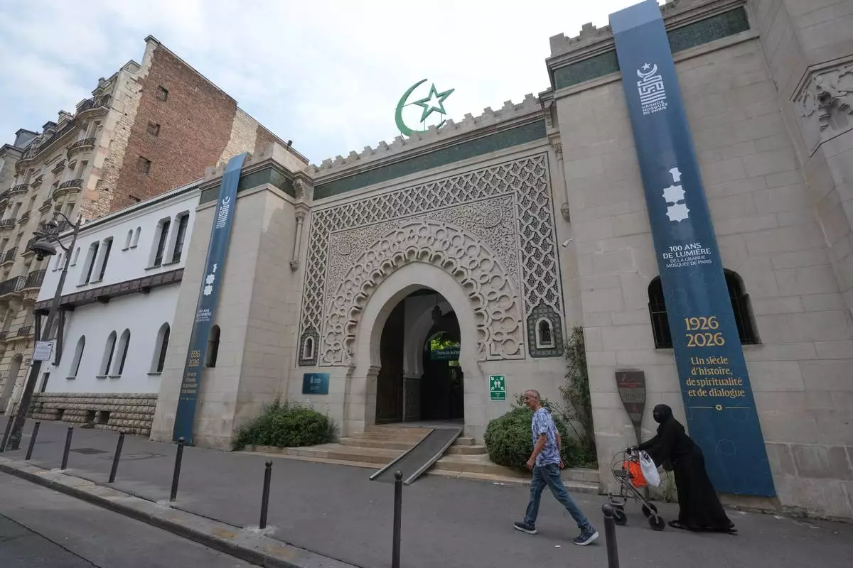 People walk past the Grand Mosque of Paris, where a banner reads, "100 years of light, a century of history, spirituality and dialogue" marking its 100th anniversary, Friday, July 17, 2026. (AP Photo/Michel Euler)