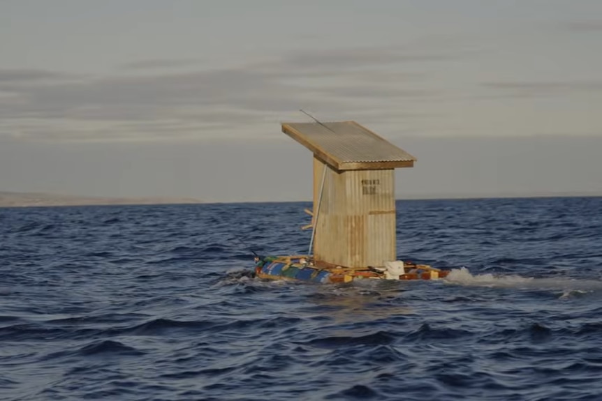 An old fashioned outback toilet floats across the ocean aboard a homemade barge