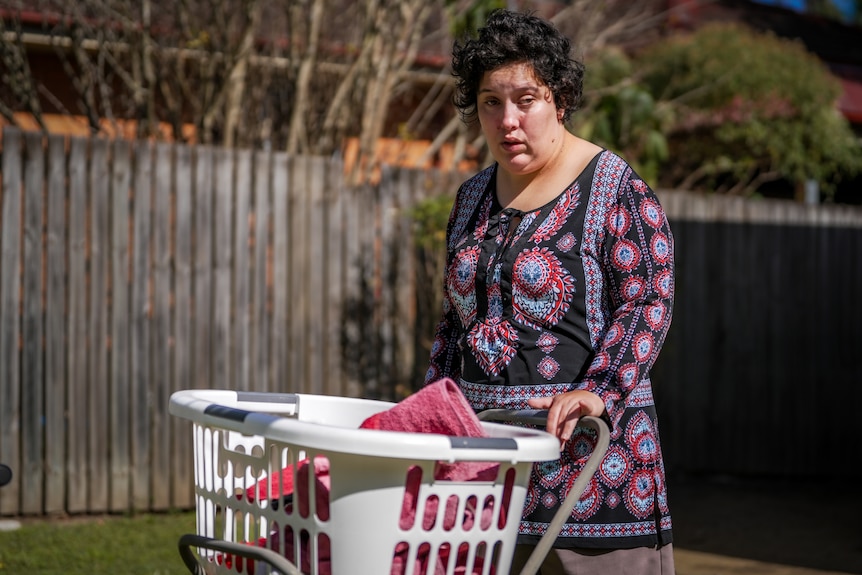 A woman with short brown hair wearing a black and red patterned dress with a laundry basket.