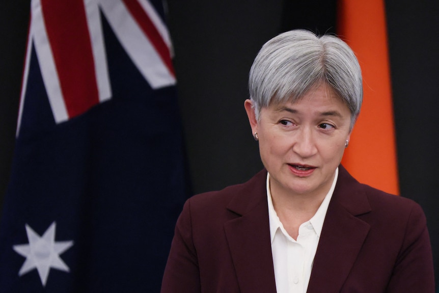 A woman stands in front of the Australian flag.