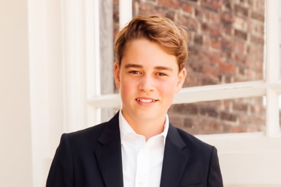 George in a black suit and white shirt, smiling.