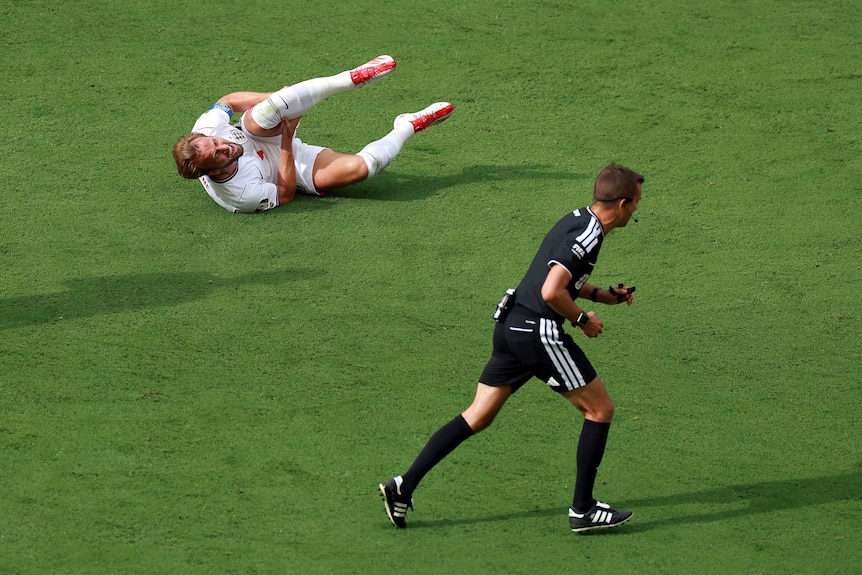 Harry Kane looks at the referee while holding his leg on the floor.