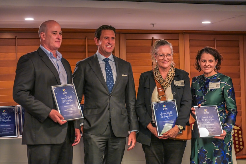 One man and two women each holding awards with a man in a suit and tie