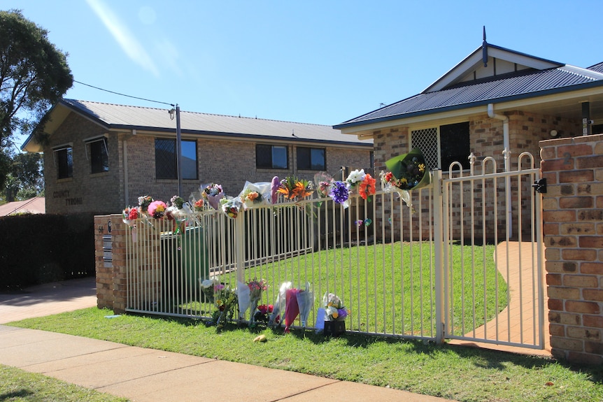 Floral tributes on a fence outside a brick home.