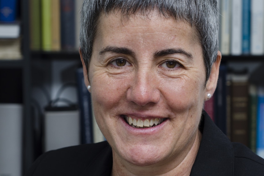 Woman with short hair and wearing a dark top smiles at the camera.