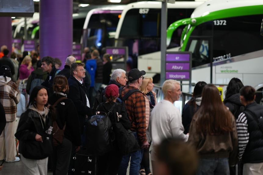 Crowds of people wait in lines for buses at Southern Cross station.