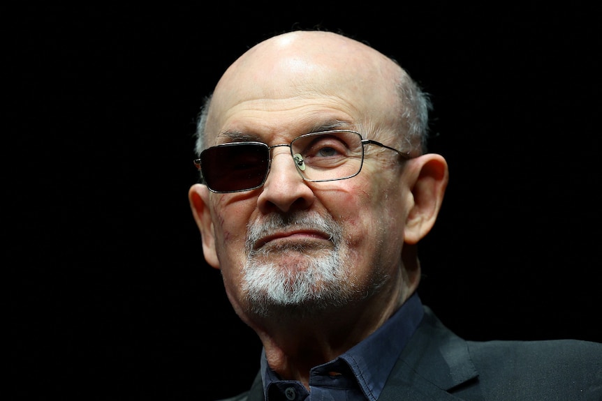 Salman Rushdie faces the camera with one of the lenses of his glasses blacked out.