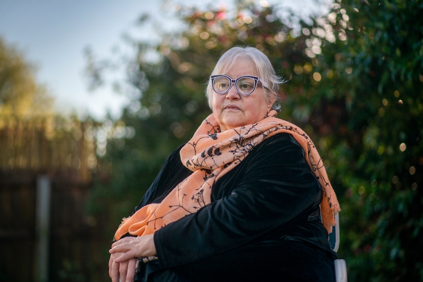Woman wearing glasses and scarve sits outside 