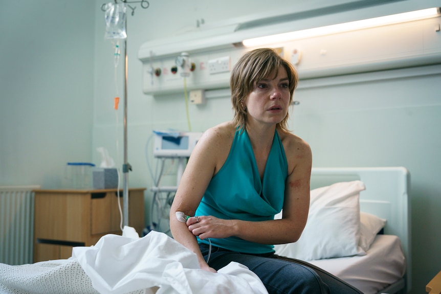 A woman in a blue top sits in a hospital bed.