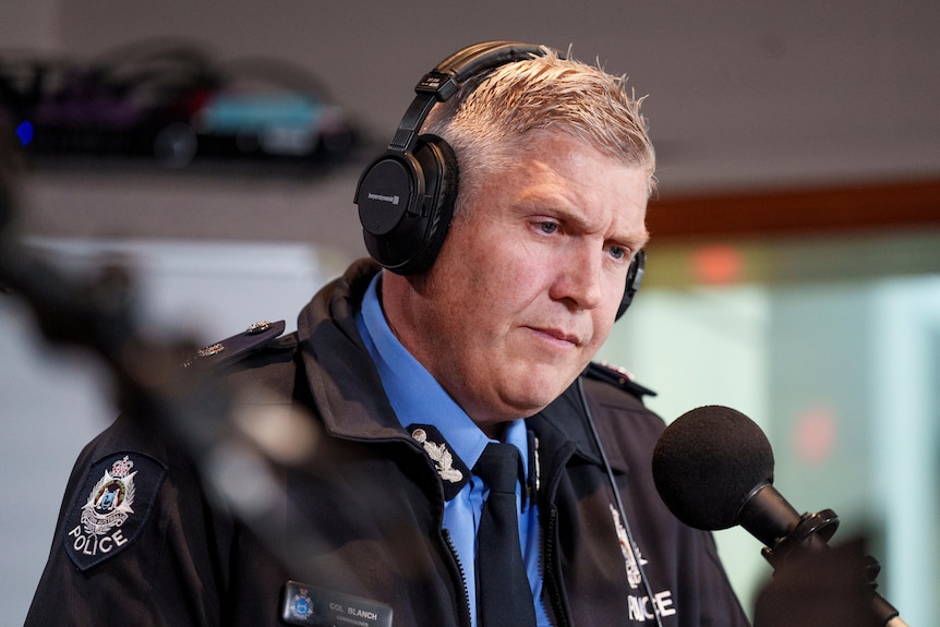 A middle-aged, uniformed policeman wears headphones while in a radio studio.