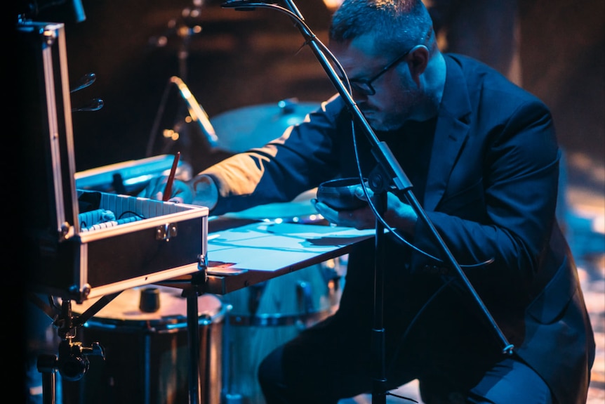 Adam Manning plays percussion on a darkened stage, with microphones around.