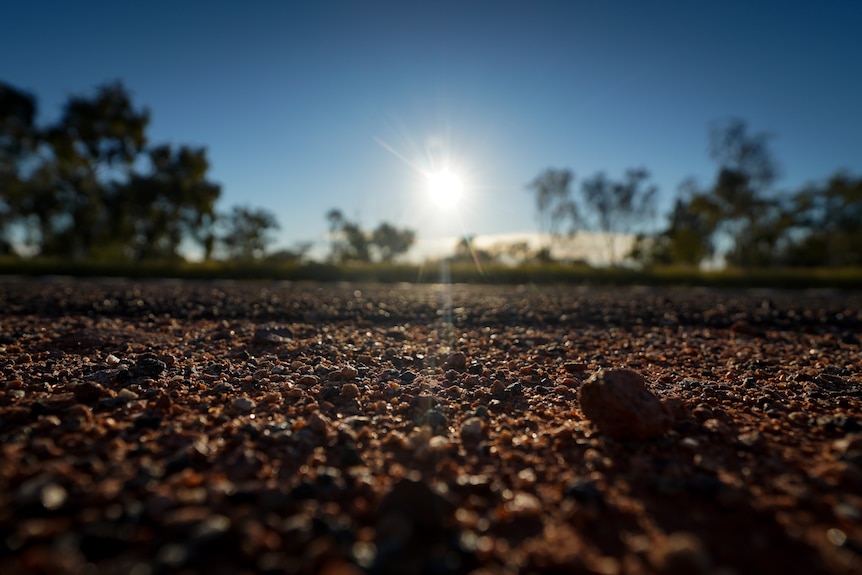 A gravel road close up, brown pebbles in view as the sunlight pours down on the bitumen.
